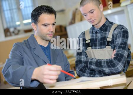 Giovane apprendista con insegnante lavorando sul pezzo di legno Foto Stock