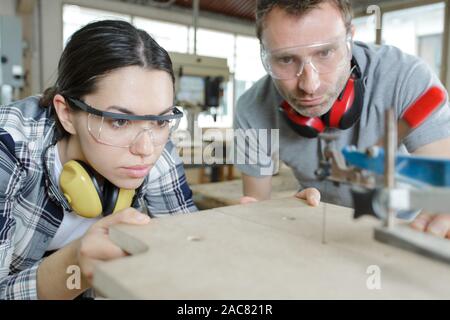 Due moderni artigiani che lavorano insieme utilizzando macchine in officina Foto Stock