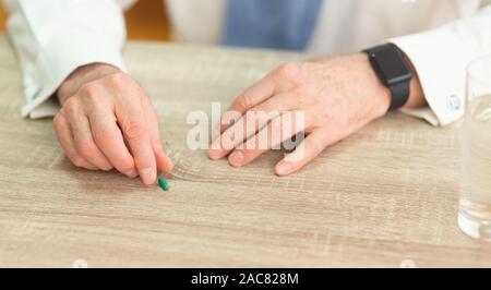Uomo anziano con le mani smartwatch prendendo pillola dalla tabella, panorama Foto Stock