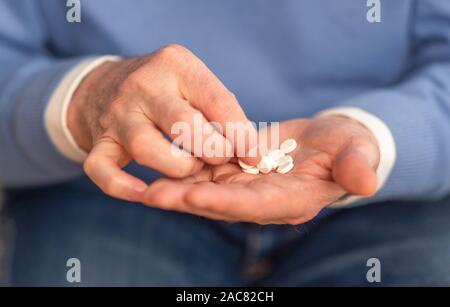 Uomo anziano con le mani in mano il prelievo di una pillola da manciata di compresse Foto Stock
