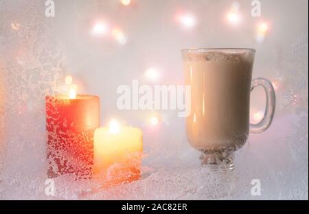 Rosso e giallo candele su sfondo bianco. Tazza di caffè all'interno della casa con la brina sul vetro e luci di noi un simbolo di vacanza. Foto Stock