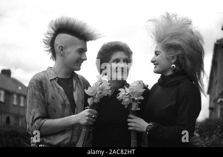 1987, "giorno dell'...due giovani adulti in 'punk' capelli mode dell'epoca, in piedi fuori in una strada presente la loro madre con i fiori in questo giorno speciale, Inghilterra, Regno Unito. Foto Stock