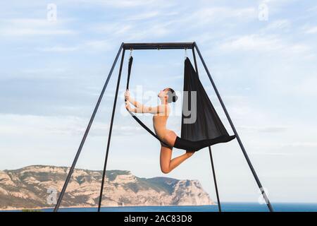 Donna pratica fly dance gravità lo yoga pone in una amaca all'aperto con vedute delle montagne. Vita sana, sport estivi. Foto Stock