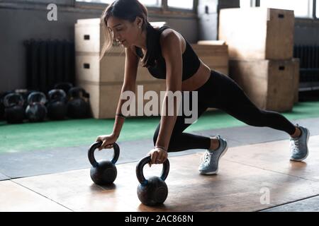 Slim brunette facendo push-up esercizi su kettlebells. Cross fit training Foto Stock