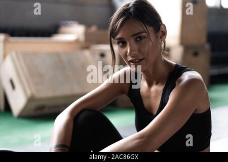 Giovane donna seduta sul pavimento dopo il suo allenamento e guardando verso il basso. Atleta femminile prendendo riposo dopo un allenamento fitness Foto Stock