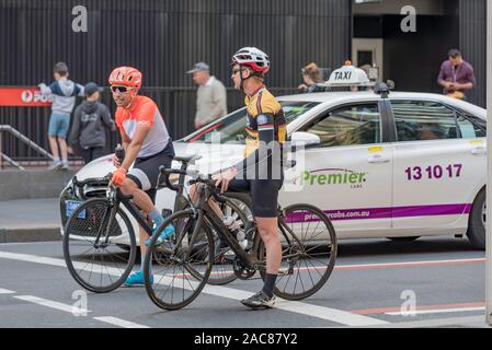 Due persone di mezza età maschio persone su biciclette arrestato e in attesa ad un semaforo nei pressi di un taxi su una strada di città nel CBD di Sydney, Australia Foto Stock