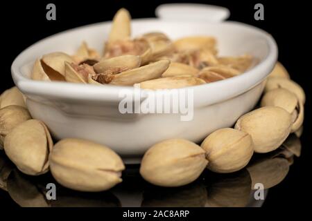 Sacco di tutta la salatura pistacchio in bianco piccolo vaso in ceramica isolata sul vetro nero Foto Stock