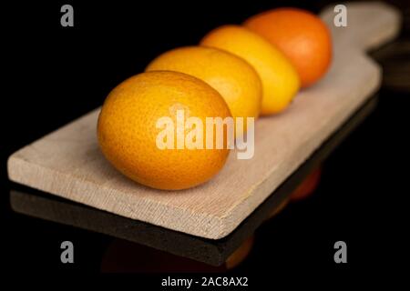 Il gruppo di quattro tutta la gustosa orange kumquat sul tagliere di legno isolata sul vetro nero Foto Stock