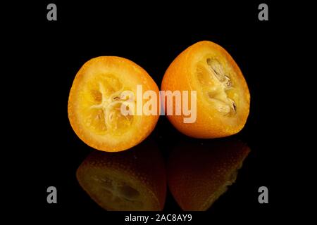 Gruppo di due metà di gustoso orange kumquat isolato sul vetro nero Foto Stock