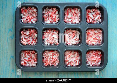 Christmas rosso e bianco strisce caramella alla menta piperita all'interno di piazze su sfondo di legno. All'interno di un vassoio metallico. All'interno del centro di una foto. Foto Stock