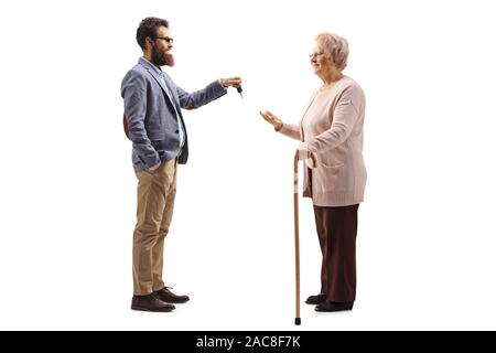 Lunghezza piena ripresa del profilo di un uomo barbuto dando le chiavi dell'auto per una donna anziana con un bastone da passeggio isolati su sfondo bianco Foto Stock