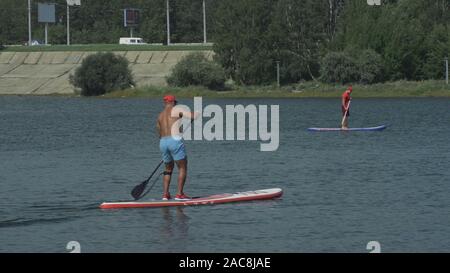 Atleta in stand up paddleboard sup azienda scheda pala fino in aria in successo su paddleboarding gara. SUP tavola da surf surf, sport d'acqua. Foto Stock