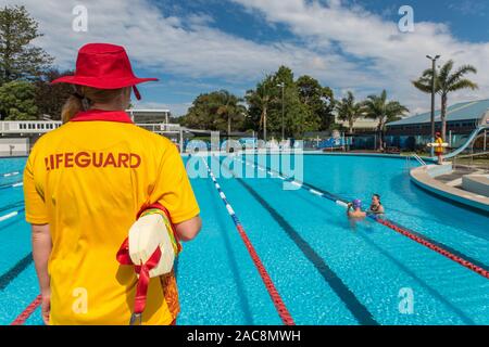 Un bagnino femmina veglia su due nuotatori in una piscina pubblica in una luminosa giornata estiva con un altro bagnino di distanza Foto Stock