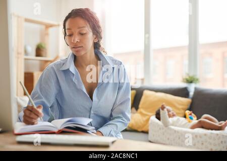 Ritratto di afro-americano di madre di lavoro utilizzando il computer portatile o studiare con il bambino in background, spazio di copia Foto Stock