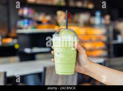 Mano che tiene un bicchiere di tè verde Frappe con gelato al cafe Foto Stock