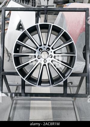 A due di colore nero e argento verniciata in lega di alluminio ruota è montato su un telaio speciale durante il processo di essiccazione in una camera in una carrozzeria di veicolo in officina Foto Stock