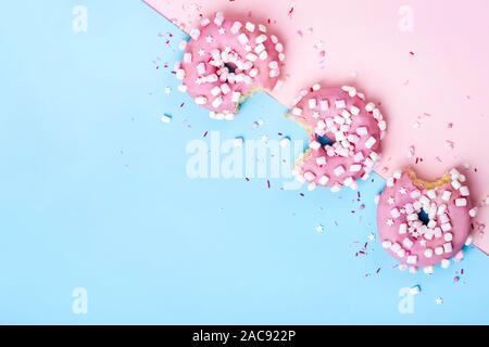 Layout creativo fatto di rosa morso ciambelle e sfondo geometrico. Concetto di cibo. Foto Stock