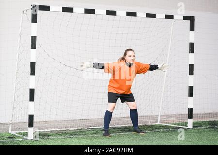 Femmina giovane portiere in uniforme di sport e guanti outsretching le braccia mentre in piedi nella porta pronto a catturare la sfera Foto Stock