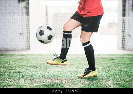 Sezione bassa della femmina e giovane giocatore di calcio con pallone da calcio su piede formazione sul campo verde a Stadium Foto Stock