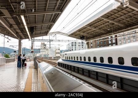 Il treno Shinkansen giapponese o Shinkansen con partenza dalla Stazione di Osaka con passeggeri con bagagli in attesa sulla piattaforma guardando a telefoni cellulari Foto Stock