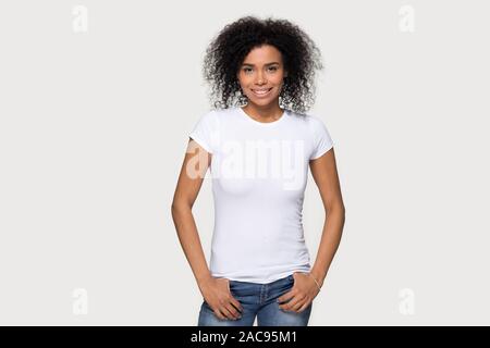 Sorridente americano africano donna in jeans e fustellato t-shirt bianca con parte anteriore mock up, attraente giovane femmina dimostrare vestiti modello di progettazione dello spazio di copia Foto Stock