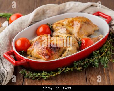 Le due carcasse fritto di pollo in una ciotola, mandrini cotta in un forno con pomodori, con crosta croccante su legno marrone scuro tavolo rustico, vista laterale Foto Stock