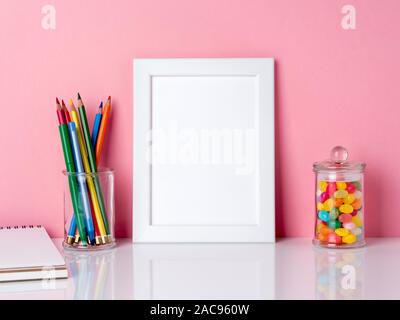 Vuoto telaio bianco e pastello in barattolo, candys su un tavolo bianco contro la parete rosa con spazio di copia Foto Stock