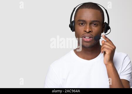 Giovani parlando operatore di supporto, call center lavoratore in cuffia, gravi African American uomo in cuffie con microfono guardando la telecamera, isolato Foto Stock