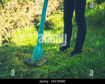 Una giovane donna è il taglio del prato utilizzando un decespugliatore di erba Foto Stock