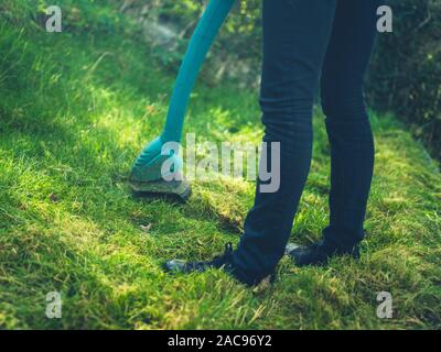 Una giovane donna è il taglio del prato utilizzando un decespugliatore di erba Foto Stock