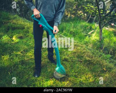 Una giovane donna è il taglio del prato utilizzando un decespugliatore di erba Foto Stock