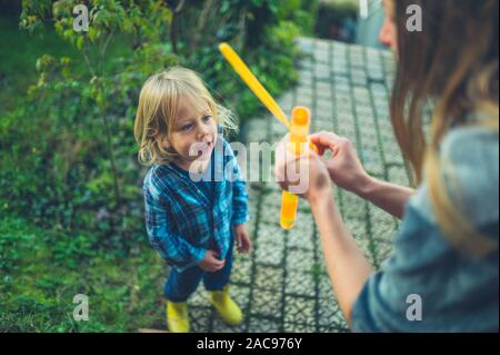 Un piccolo bimbo è soffiare bolle nel giardino con la sua madre Foto Stock