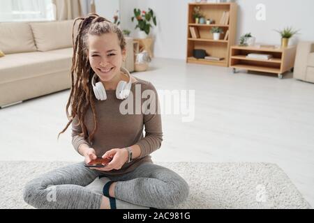 Allegro giovane donna attiva con le cuffie utilizza lo smartphone Foto Stock
