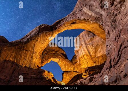 Chiaro di Luna e la luce artificiale si combinano per illuminare il doppio arco in Arches National Park nello Utah. Foto Stock
