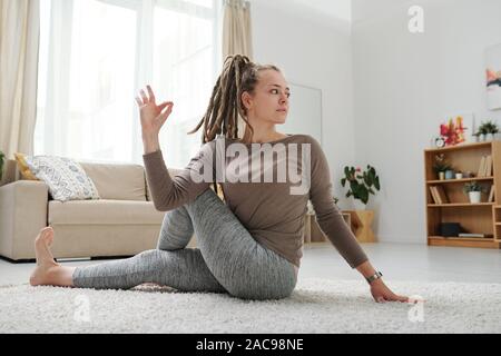 Giovani femmine con dreadlocks seduta sul pavimento in una delle posizioni di yoga Foto Stock