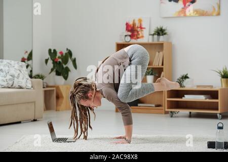 Bella ragazza con dreadlocks in piedi sulle mani nella parte anteriore del computer portatile Foto Stock