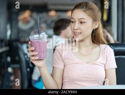 Donna che mantiene un bicchiere di mirtillo frullati in una caffetteria Foto Stock