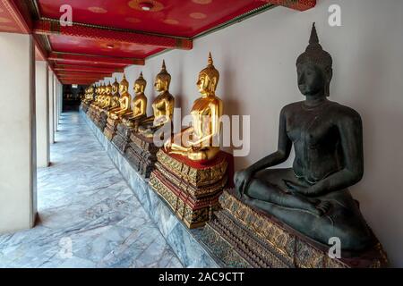 Una scultura del buio e molti golden Buddha seduto in posizione del loto in una fila. Pavimento in marmo e soffitto rosso. Una fila di colonne. Foto Stock