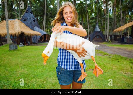 Giovane donna felice tenere in mani funny farm pet - grande bianco oca domestica. Gita di Un Giorno sul le vacanze estive in famiglia con i bambini. Foto Stock