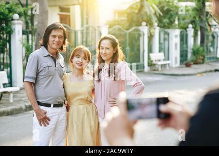 Felice asiatica di mezza età i genitori in posa con la loro figlia adulta per foto sullo smartphone Foto Stock