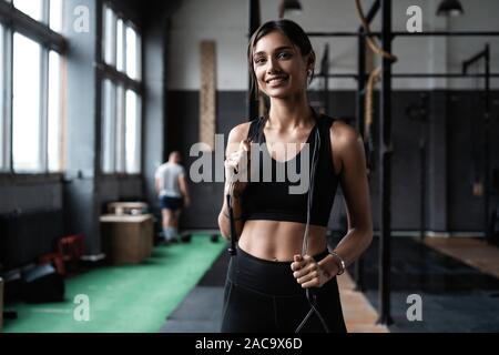 Montare e donna sana in piedi alla palestra con corda da salto. Sportive riposo dopo l'allenamento. Foto Stock