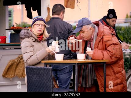 Paio mangiare fagioli stufati servite in tazze monouso a alimentare tabella di stallo durante il riposo. Mercatino di Natale a Zagabria, Croazia Foto Stock