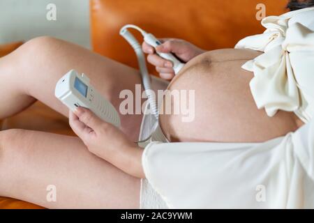 Donna incinta utilizzando droppler fetale dispositivo per ascoltare il suo bambino heartbeat Foto Stock