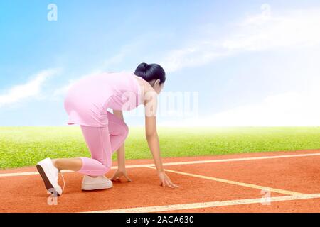 Vista posteriore di Asian runner donna pronto a correre sulla pista da corsa con un cielo blu sullo sfondo Foto Stock