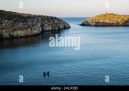 Vista serale verso Selmunet o sulle isole di Saint Paul e due uomini la pesca dalla barca, Malta Foto Stock