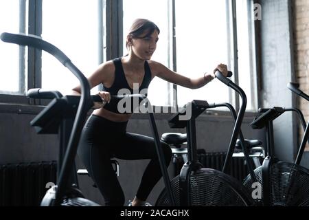 Montare la giovane donna con cyclette in palestra. Femmina Fitness utilizzando aria bike cardio allenamento in palestra Foto Stock