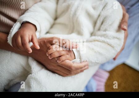 Close-up di madre mentre tiene il suo bambino con le mani in mano mentre si tiene su di lui le mani e cullano lui Foto Stock