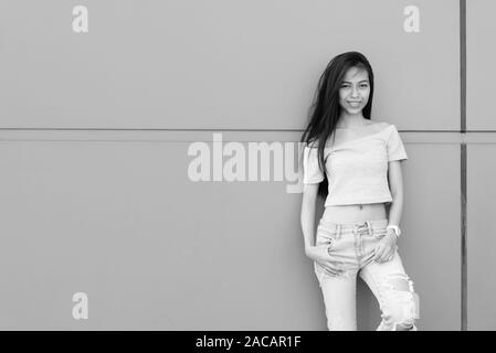 Giovani asiatici felice ragazza sorridente in posa e appoggiata contro il muro di cemento all'aperto Foto Stock