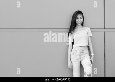 Giovani asiatici felice ragazza adolescente sorridere mentre appoggiata contro il muro di cemento all'aperto Foto Stock