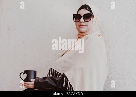 Grazioso centro Ragazza orientale nel tradizionale abbigliamento islamico, bere tazza di caffè. Carino donna araba tenendo una tazza di bevanda calda in mani Foto Stock